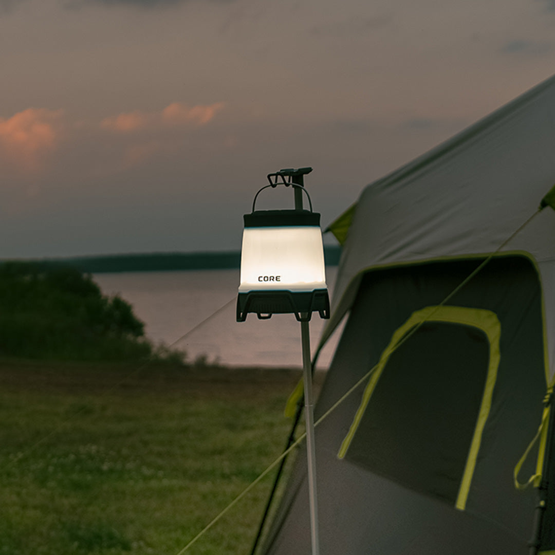 CORE 1250 Lumen Rechargeable Bluetooth Lantern glowing at dusk beside a tent, featuring adjustable brightness and durable hanging handle.