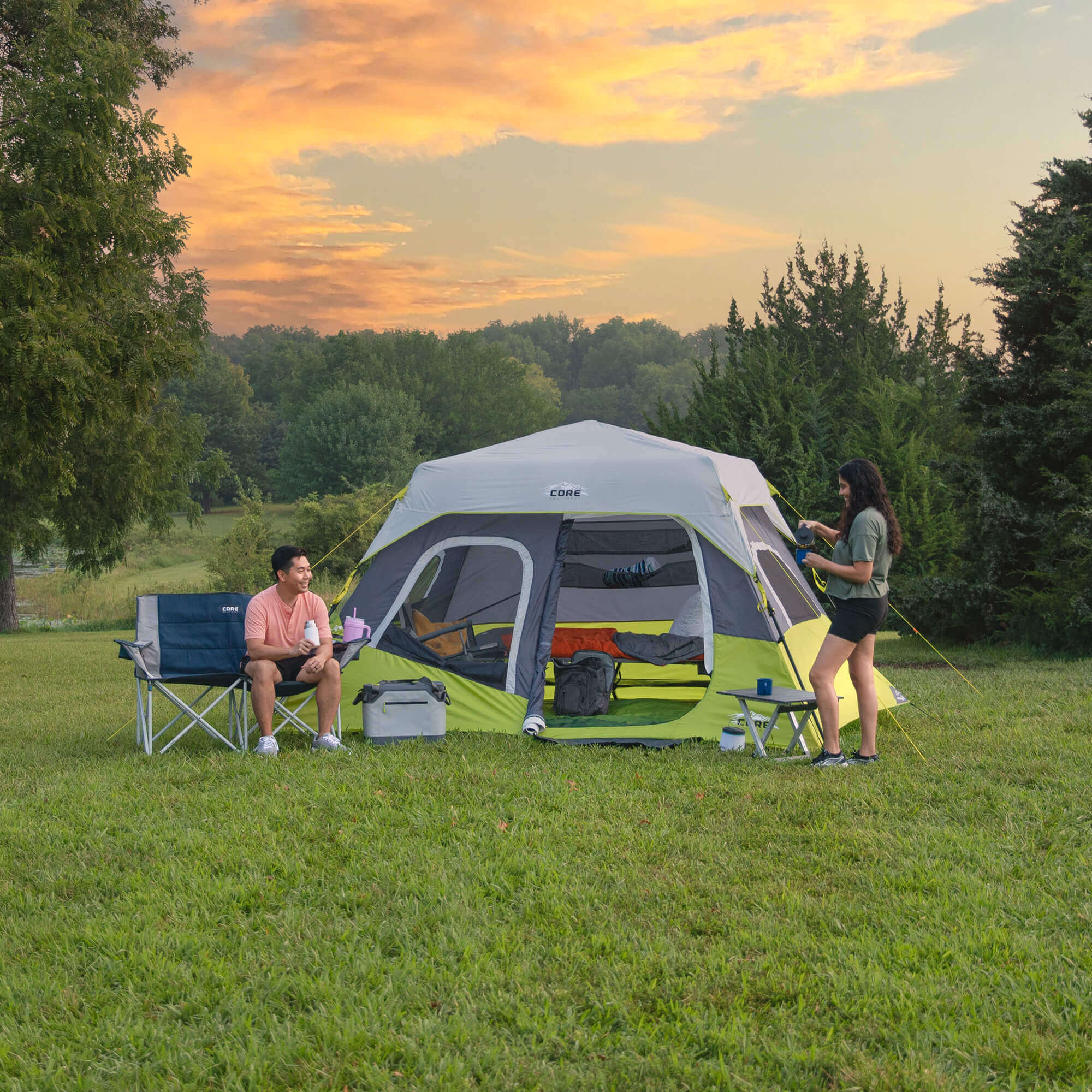 Campers outside CORE 6 person instant cabin tent in gray and green, enjoying outdoor setup at sunset in grassy field.