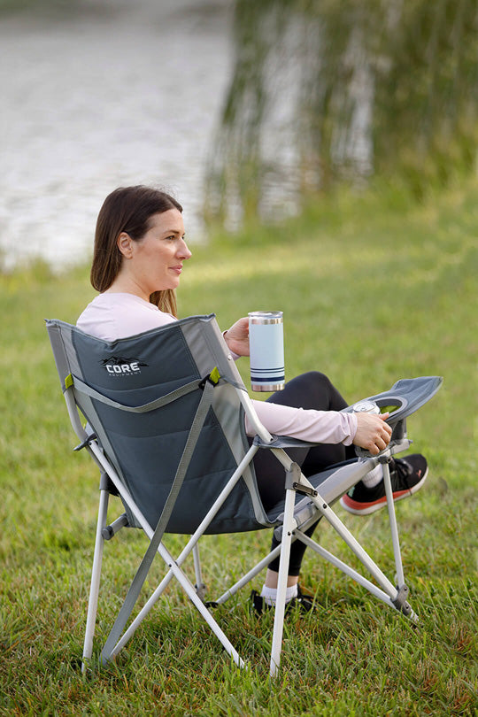 Woman sitting in a CORE tension camping chair by a lake drinking a cup of coffee.