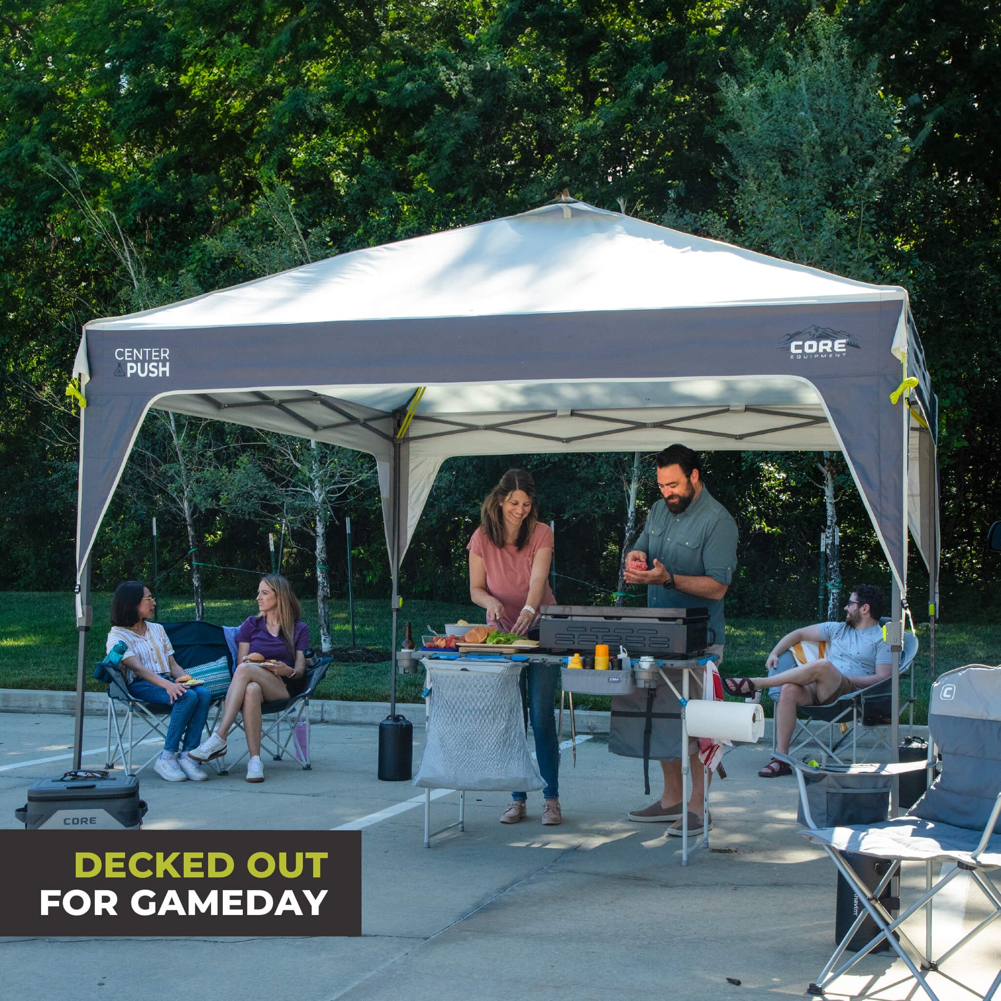 Friends relaxing outdoors under the CORE 10x10 Center Push canopy top in gray, providing shade and ventilation for gatherings.