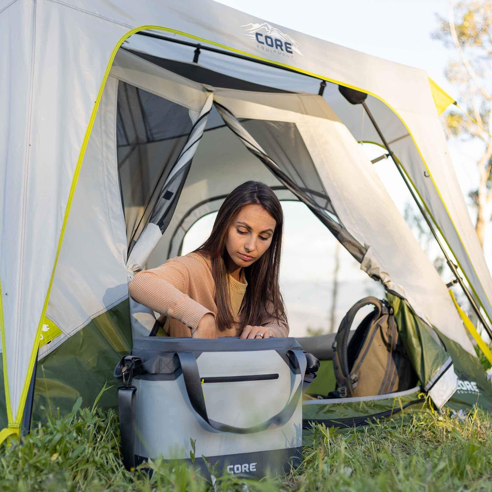 CORE 36 can performance tote cooler in gray shown outdoors beside camp tent with camper reaching into cooler, ideal for keeping drinks cold on trips.
