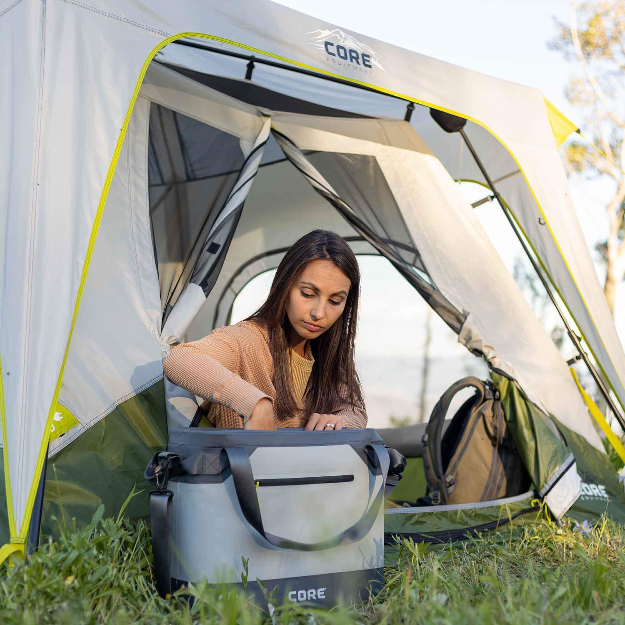 CORE 36 can performance tote cooler in gray shown outdoors beside camp tent with camper reaching into cooler, ideal for keeping drinks cold on trips.