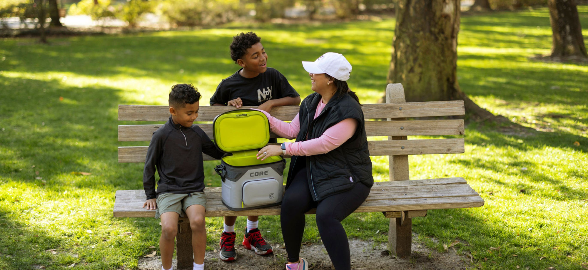 Family sitting on a park bench with a cooler bag
