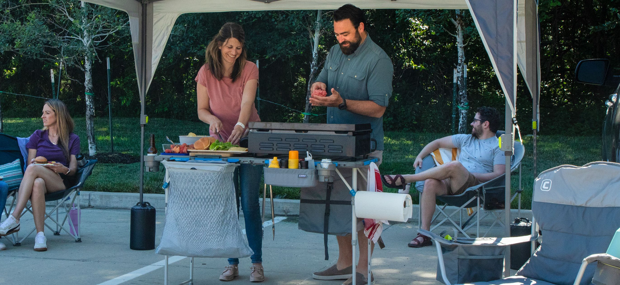 Group of people camping and cooking outdoors under a tent.