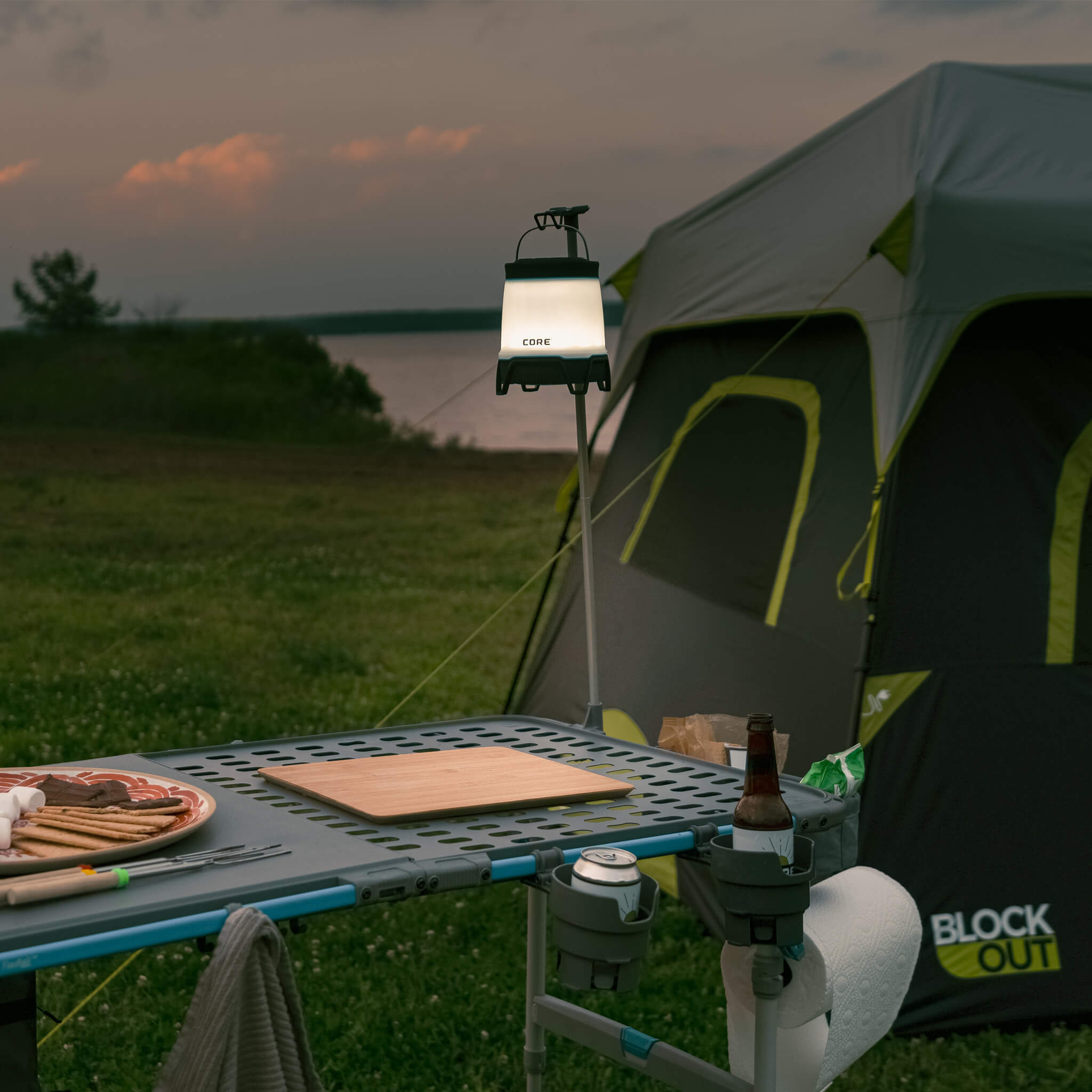 Lantern hanging from CORE lantern holder beside tent and FlexRail table at dusk, providing convenient hands-free outdoor camp lighting.