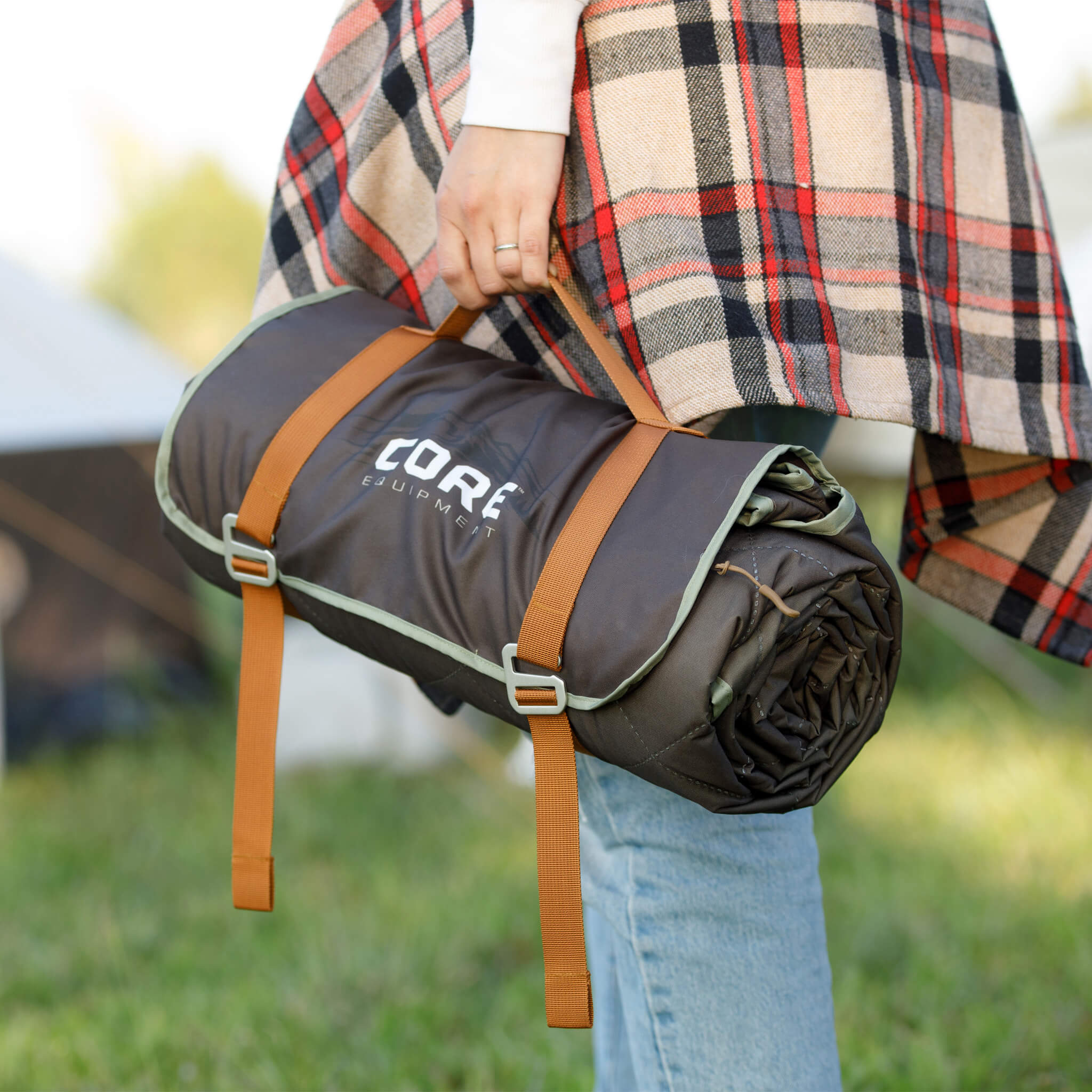 Person holding a CORE desert mosaic patterned outdoor weighted blanket in a grassy outdoor setting.