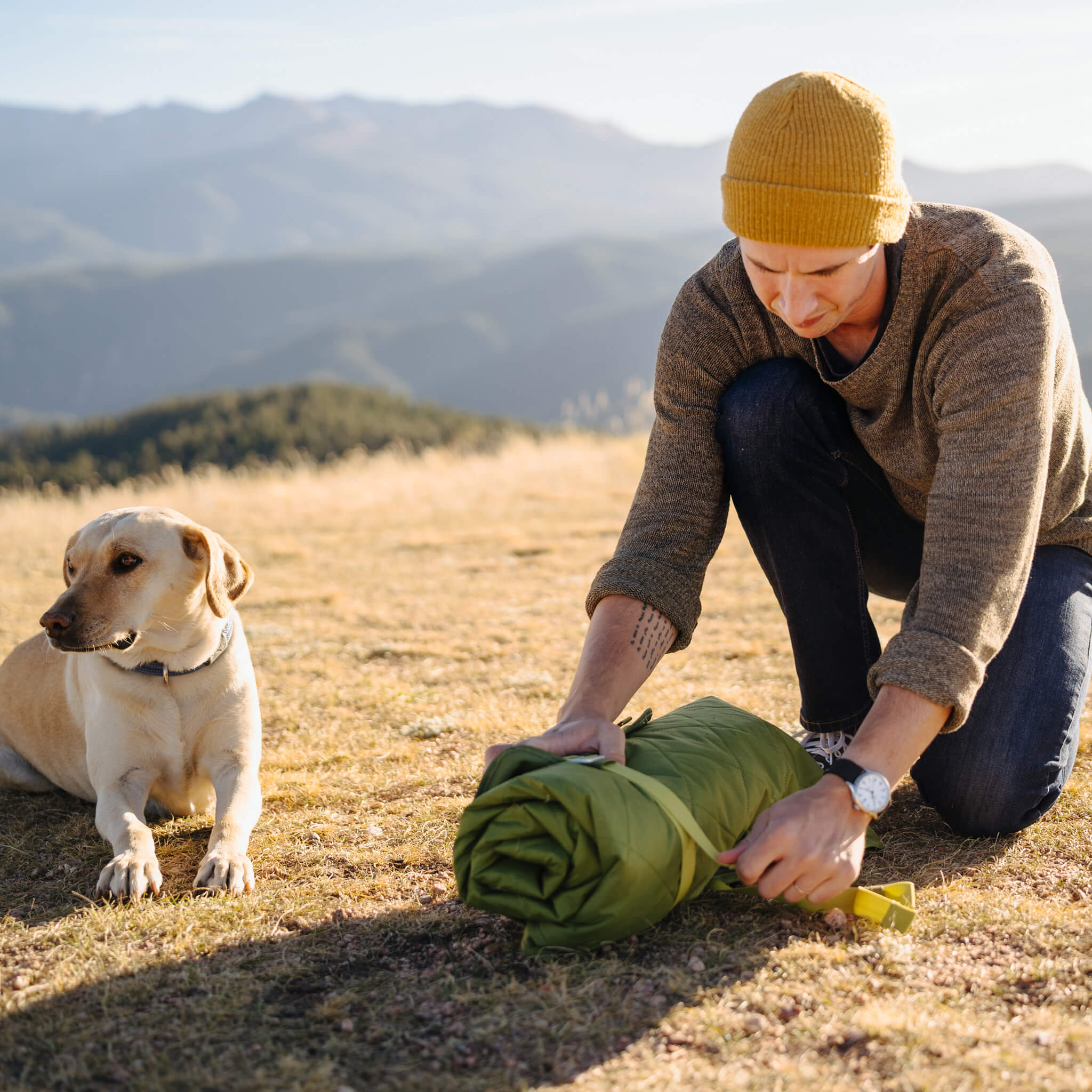 A camper with a dog using the CORE green weighted ground blanket outdoors.