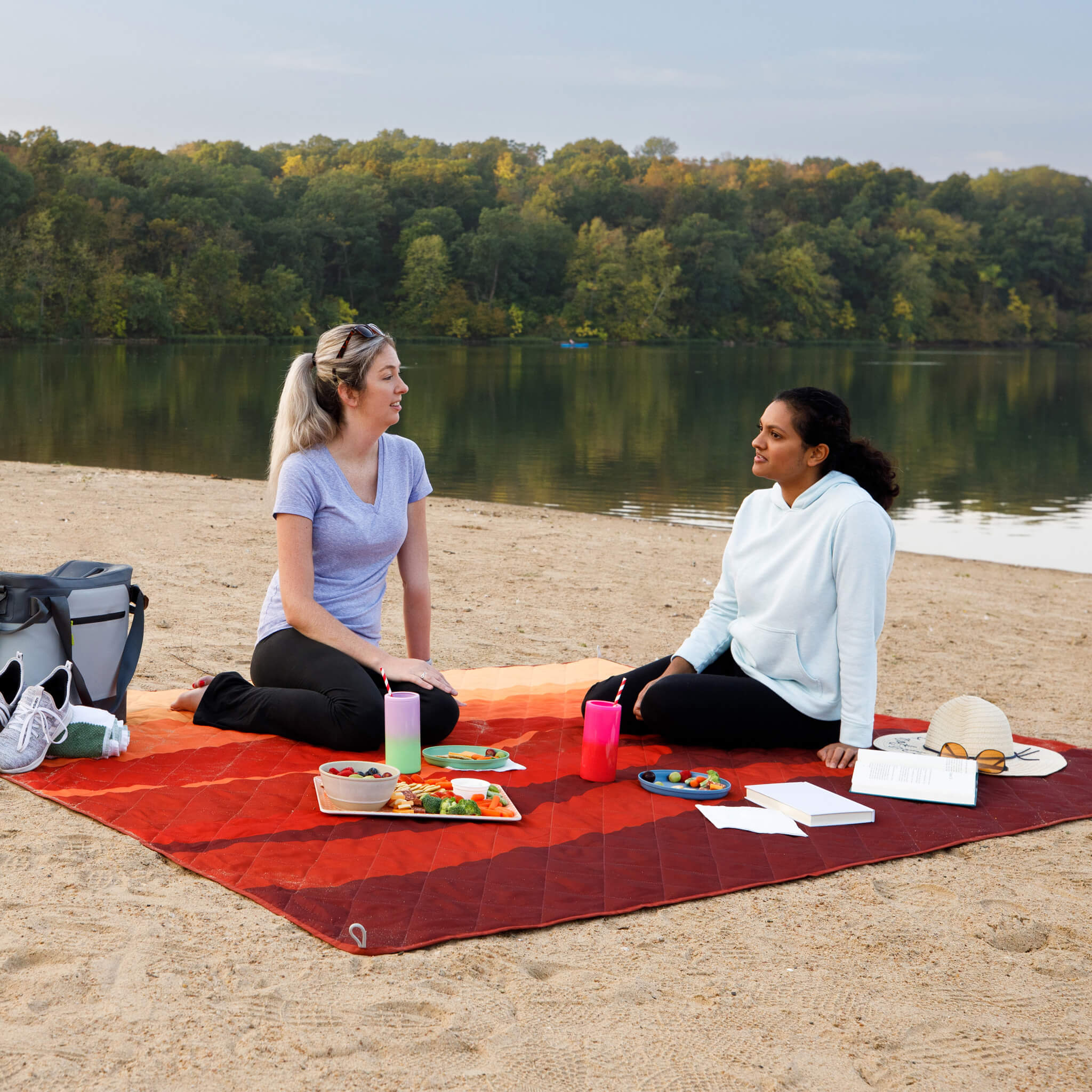 Two people having a picnic on a CORE outdoor blanket in red pattern at the beach.