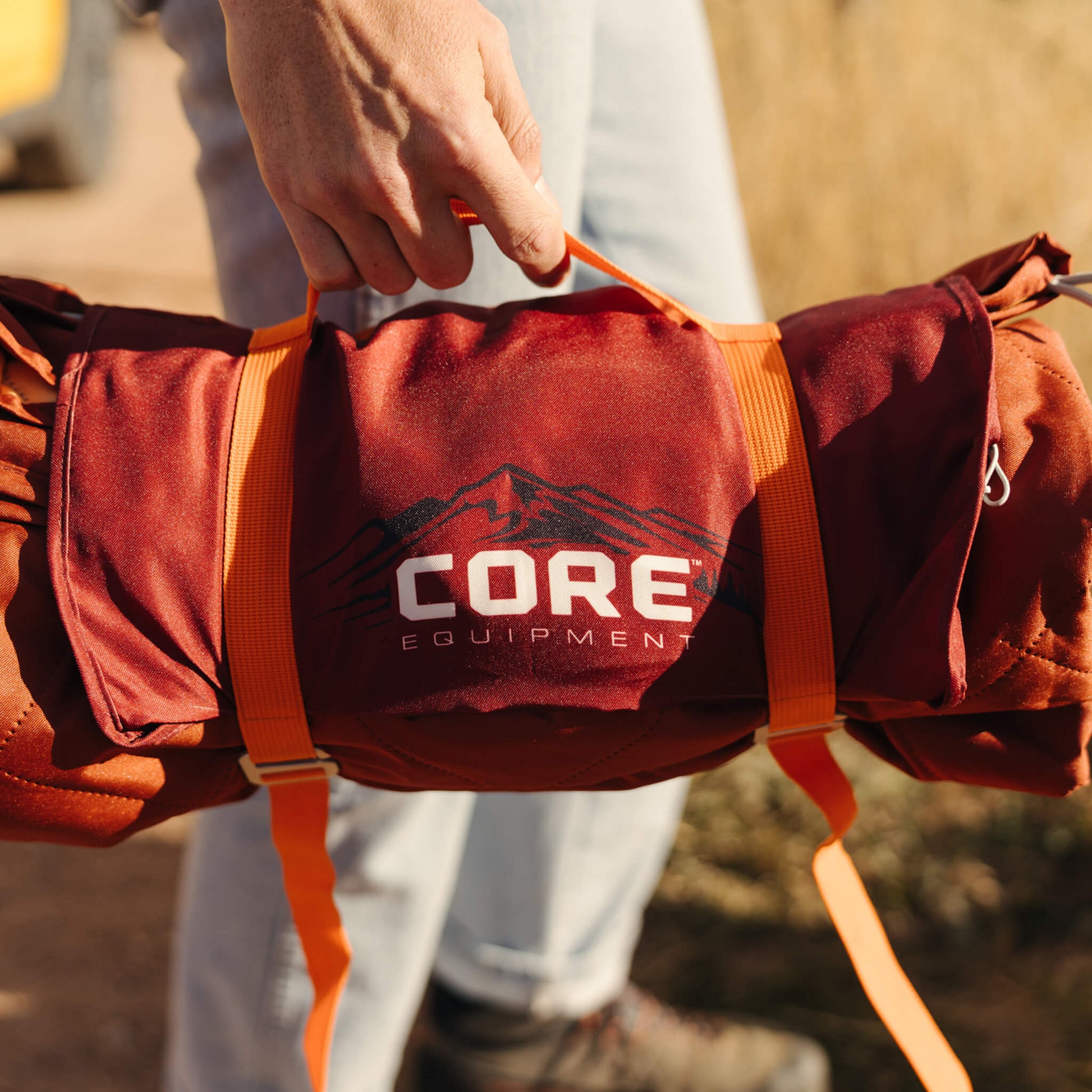CORE outdoor blanket in red pattern rolled and secured with straps.