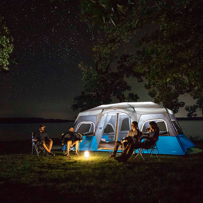 Lifestyle image of 12 person instant cabin tent with cabin light on and friends outside camping