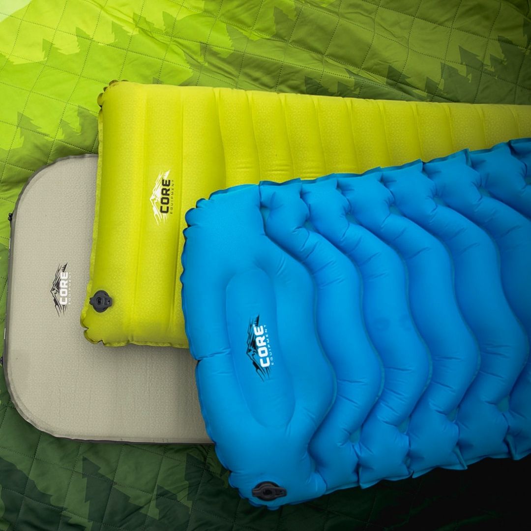 sleeping pad alt text: Three CORE Equipment sleeping pads—beige, yellow, and blue—laid out side‑by‑side on a green quilted surface, showcasing their compact inflatable design, built‑in air valves, and durable outdoor construction for camping comfort.  