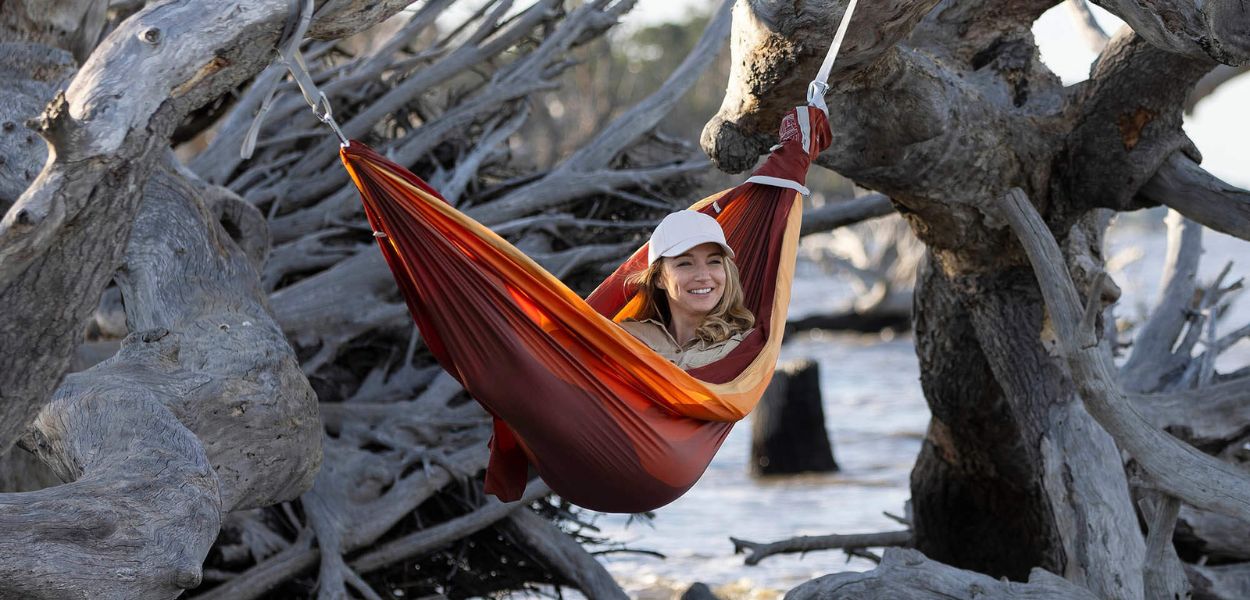 Person in a red and orange hammock hanging between trees over water