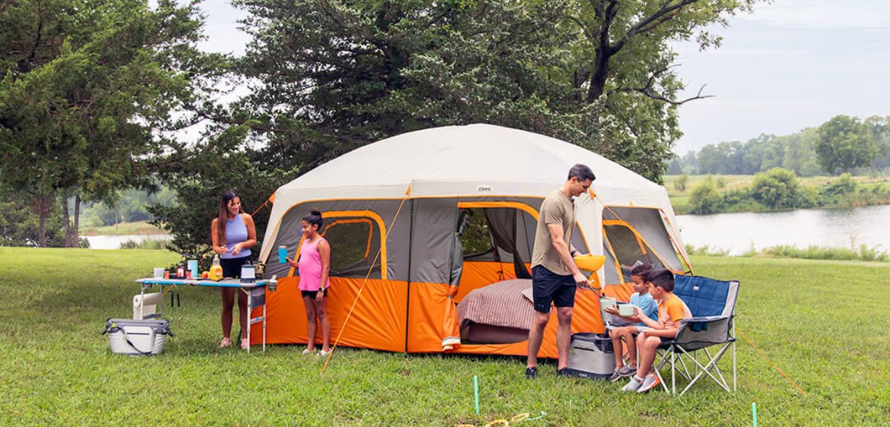Family camping outside CORE 10 person straight wall cabin tent near lake, showing spacious setup with chairs, table, and gear.
