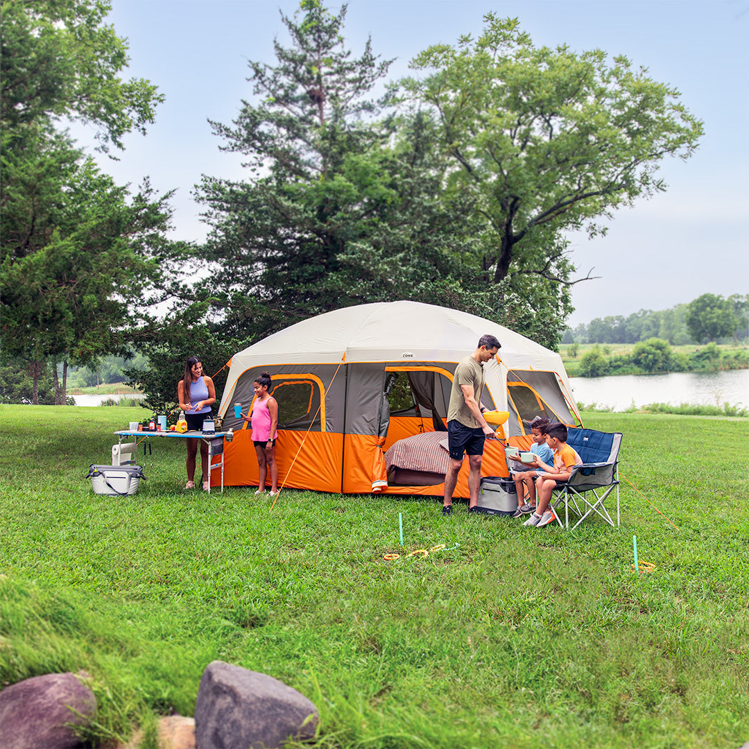 Family camping outside CORE 10 person straight wall cabin tent near lake, showing spacious setup with chairs, table, and gear.