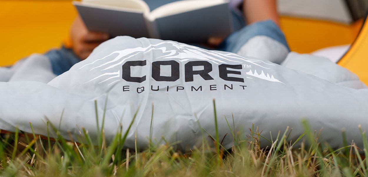 Camper reading inside a tent with the CORE 50 degree sleeping bag in gray, featuring soft lining and warm insulation.