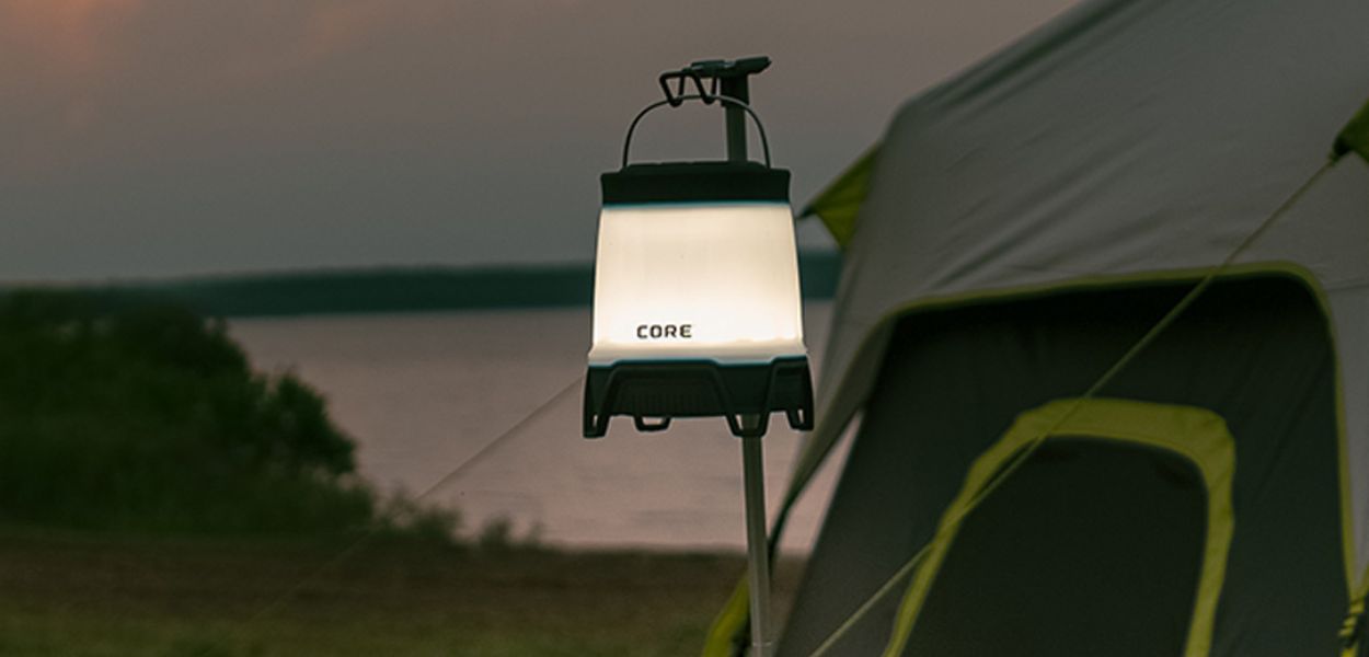 CORE 1250 Lumen Rechargeable Bluetooth Lantern glowing at dusk beside a tent, featuring adjustable brightness and durable hanging handle.
