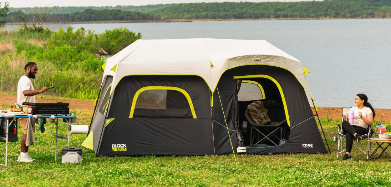 A couple camping next to a lake with a CORE tent and furniture.