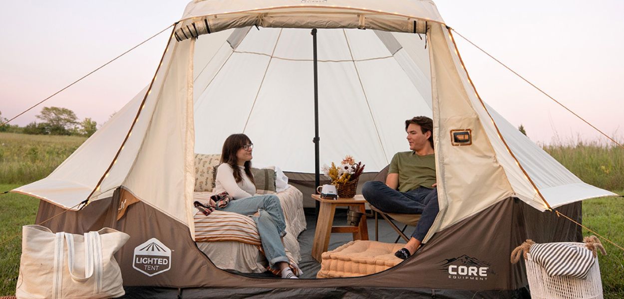 Two people relaxing inside the CORE Bell Tent with furniture and décor, showing the spacious interior and inviting setup for outdoor comfort.
