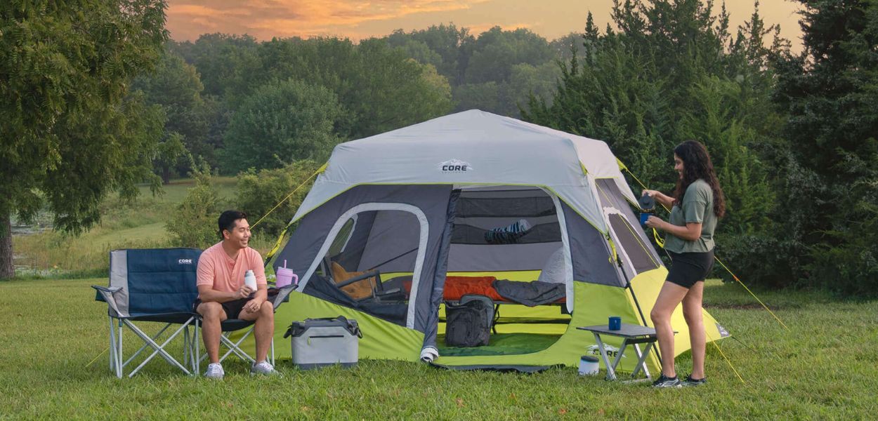 Two people camping outdoors with a CORE 6 person instant cabin tent at sunset.
