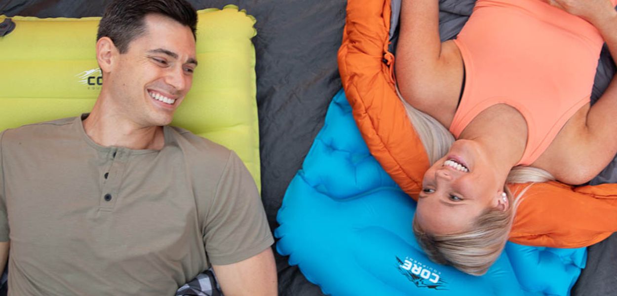 Campers relaxing on CORE Insulated Sleeping Pads in blue and green inside a tent, featuring lightweight comfort and easy inflation.