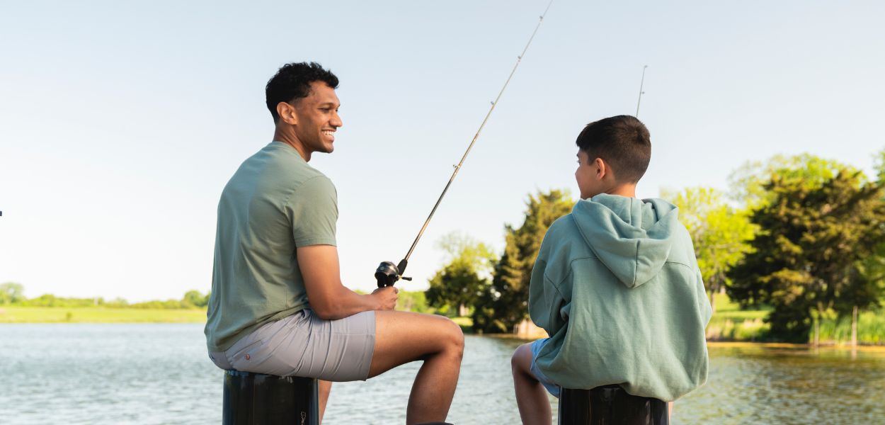 A father and son are fishing at a lake.