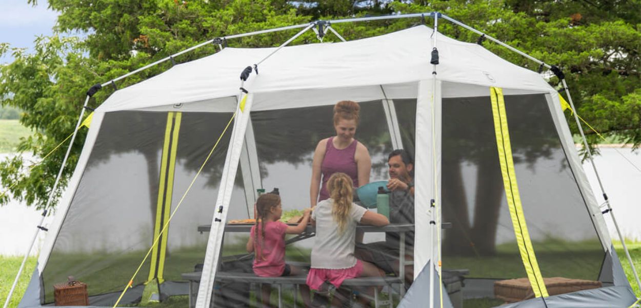 Family enjoying a meal inside the CORE 12x10 Instant Screen House, featuring mesh walls for bug protection and quick setup frame.