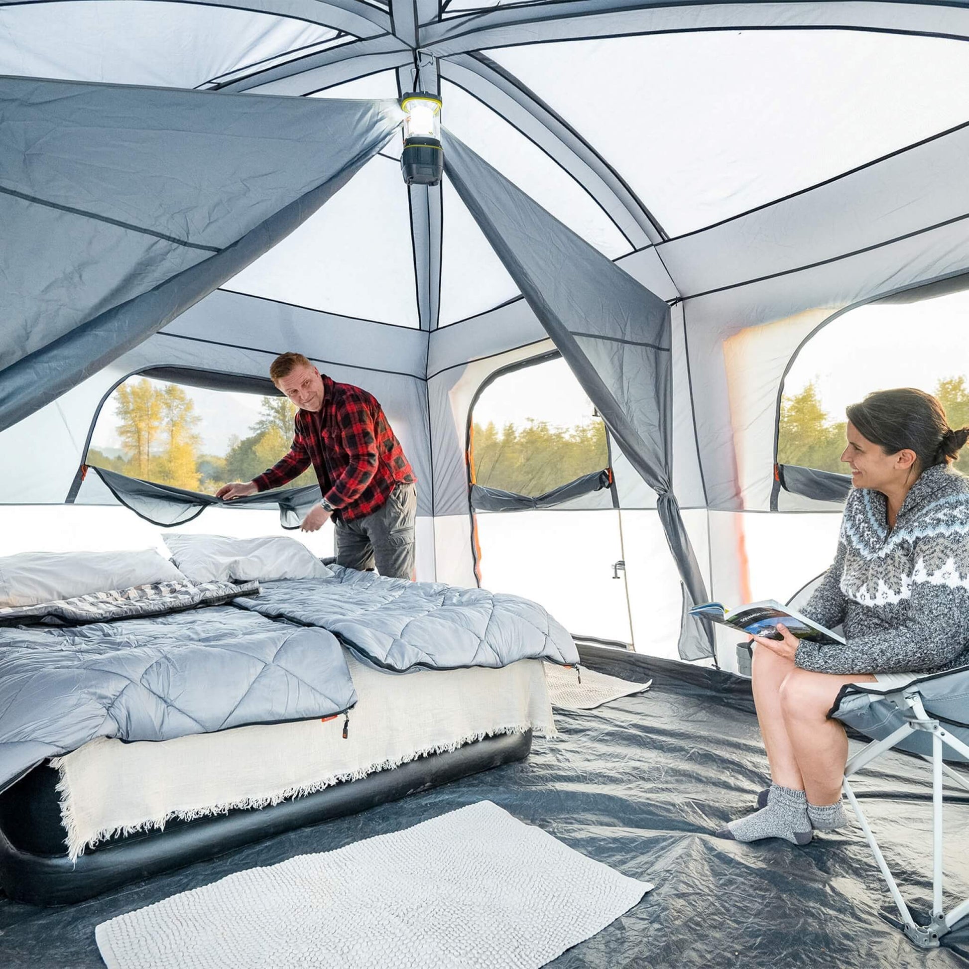 Interior of CORE 10 person straight wall cabin tent with full rainfly and camper adjusting window and another reading, showing tall ceiling and spacious setup.