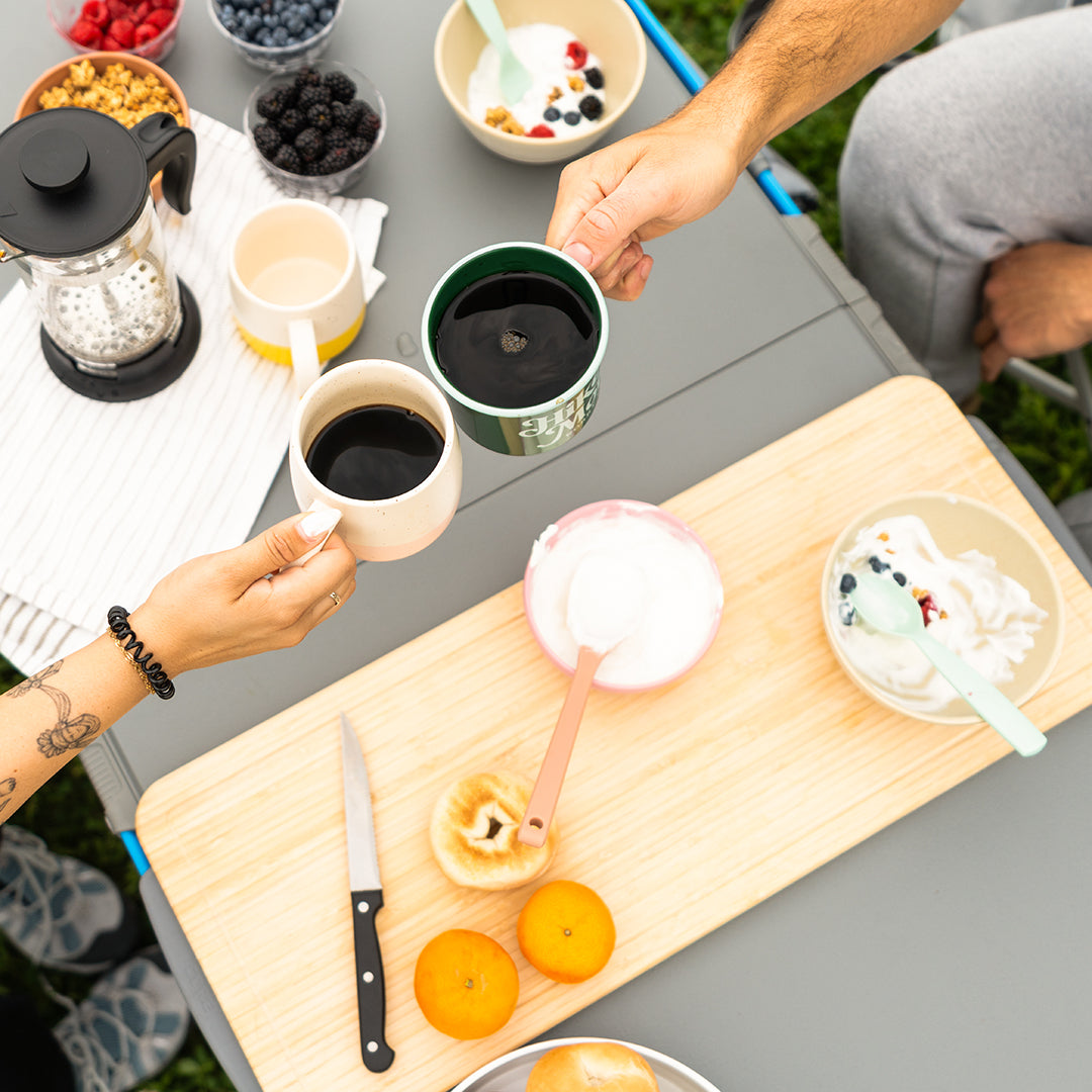 Two people are enjoying coffee at a CORE FlexRail camp table with breakfast items, including fruit and yogurt.