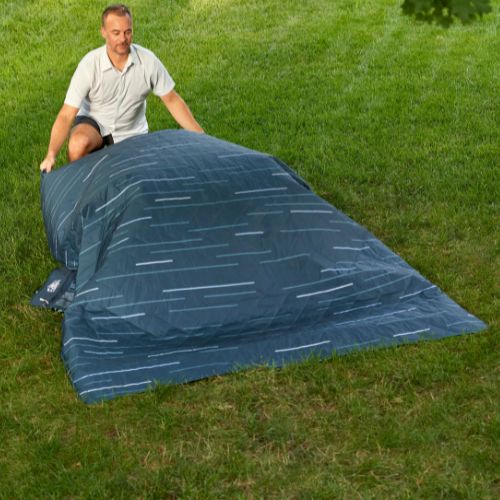 Person sitting on the CORE Staydown™ Multipurpose Blanket beside a lake, showcasing the weatherproof fabric designed for comfortable outdoor use on a variety of surfaces.