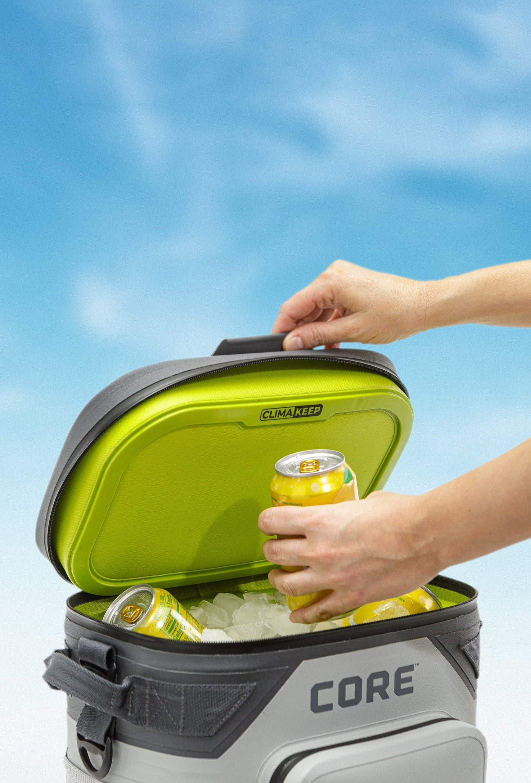 A person opening a CORE gray cooler with a blue sky background.