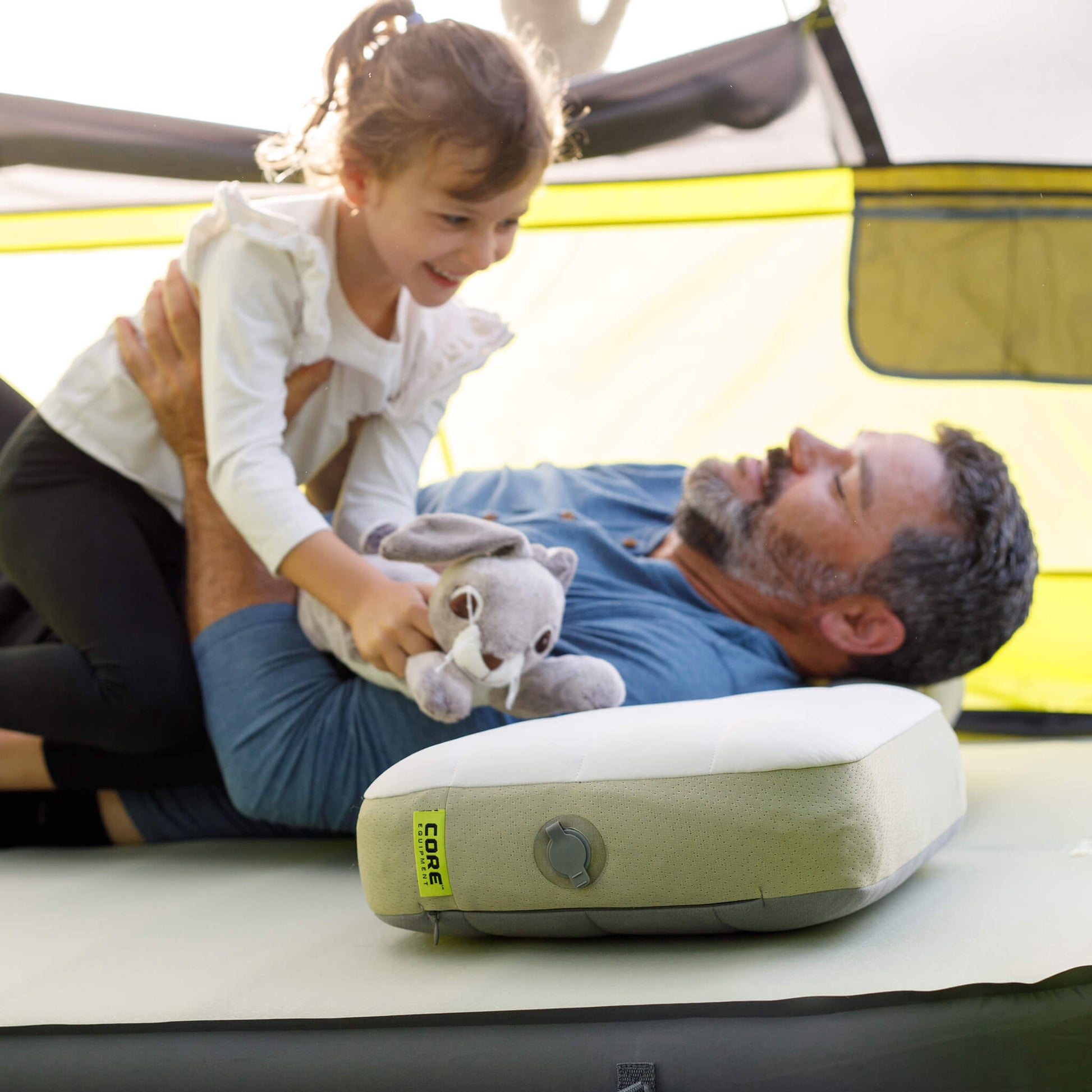 Father and daughter are lying on a CORE inflatable mattress and a self-inflating pillow inside a CORE tent.