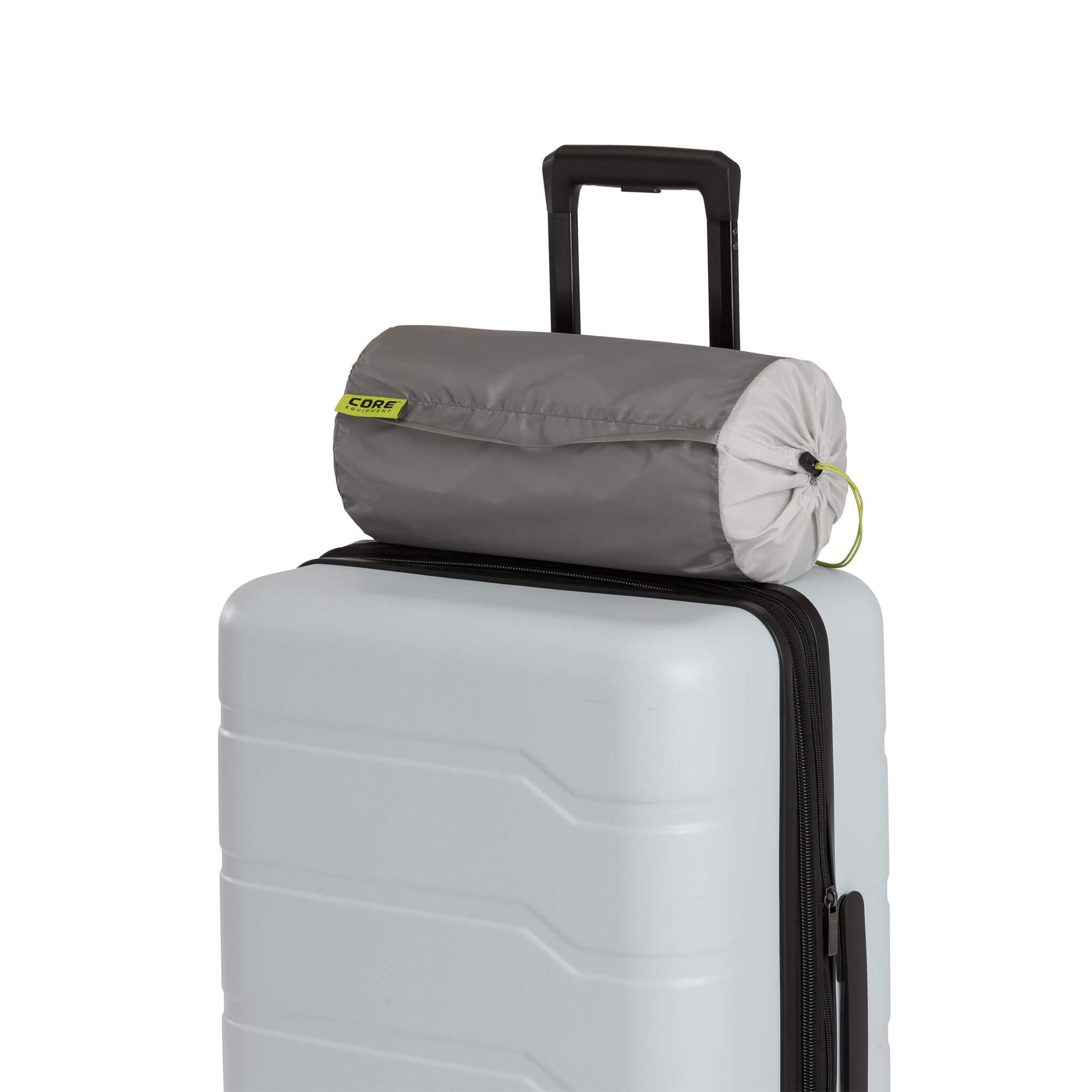 Compact gray travel pillow in a drawstring carry bag resting on top of a hard-shell suitcase with an extended handle, showing travel-ready portability and convenience.