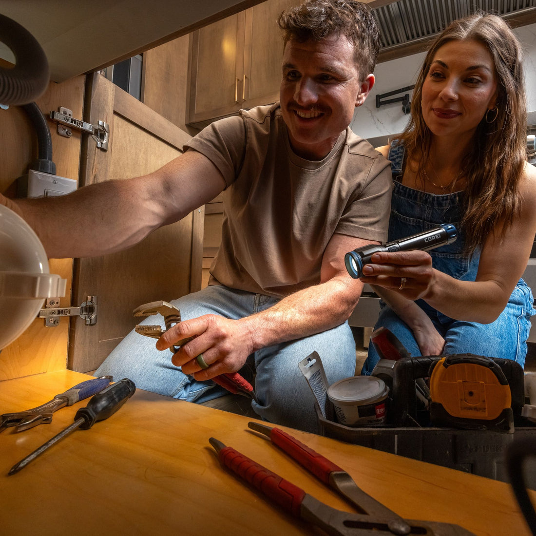 A man is working with tools while a woman points a CORE flashlight. 