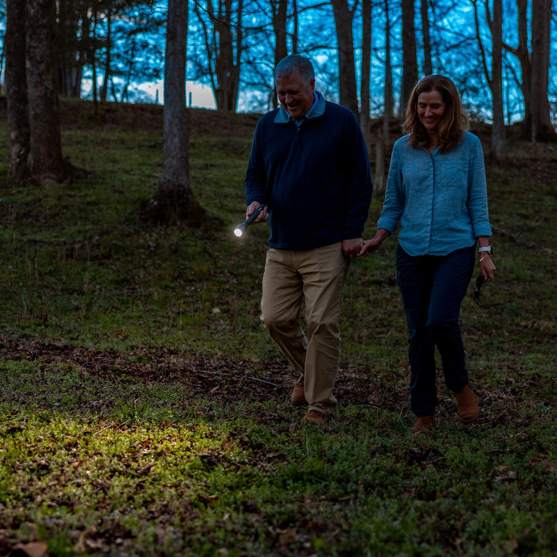 A man holds a CORE flashlight while he walks through a wooded area with a woman. 