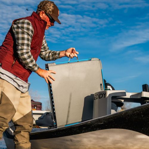 Person outdoors placing a folding camping table with CORE FlexRail carry handle onto a boat, with cooler and gear visible in a bright outdoor setting
