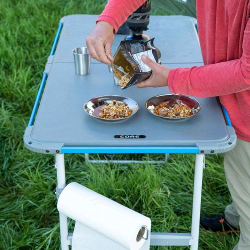 Person preparing food on a portable camping table outdoors.