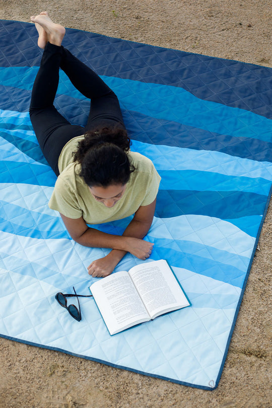 Person lying on a blue CORE Staydown Anchortech weighted blanket reading a book outdoors.