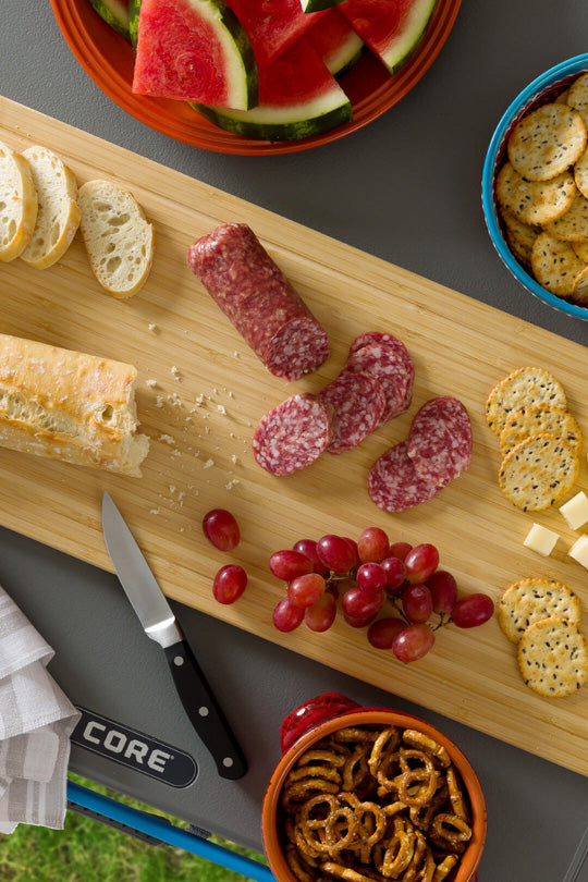 a CORE wooden cutting board with assorted snacks including salami, grapes, pretzels, and bread, attached to a CORE FlexRail table. 