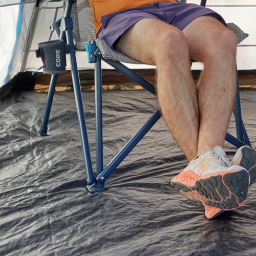 Reinforced all-terrain feet on a folding camping chair provide stable support on uneven ground, shown set up on a tent floor with crossed lower legs nearby.