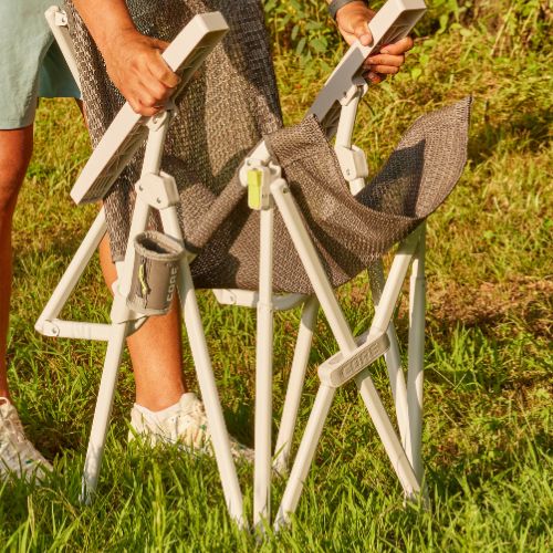 Person folding a camping chair, highlighting the sturdy locking frame and reinforced joints as the legs collapse inward for compact storage.