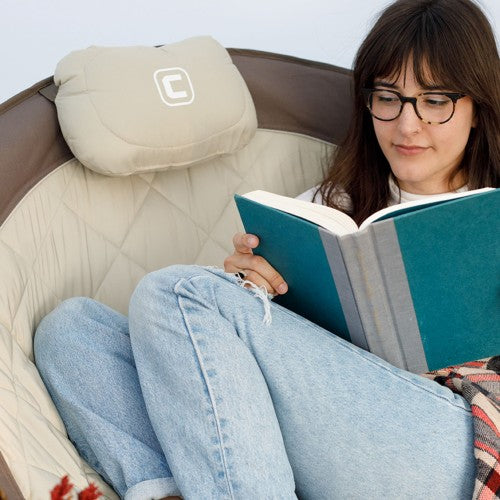 Padded, attached headrest on a gray folding outdoor chair, featuring the “CORE Equipment” logo, set against a softly blurred outdoor background with warm, natural tones.