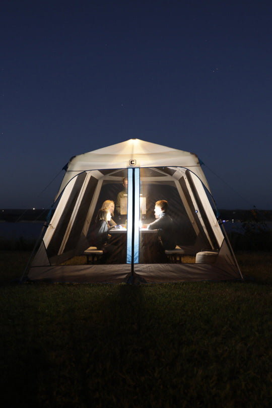 Family sitting inside a 12' x 10' lighted instant screen house at night by a body of water.