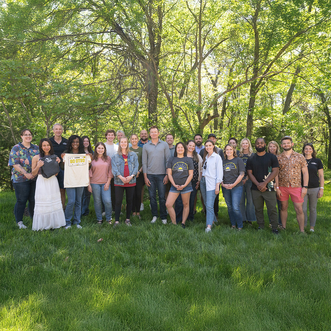 A group of CORE employees posing for a photo in a park with trees in the background
