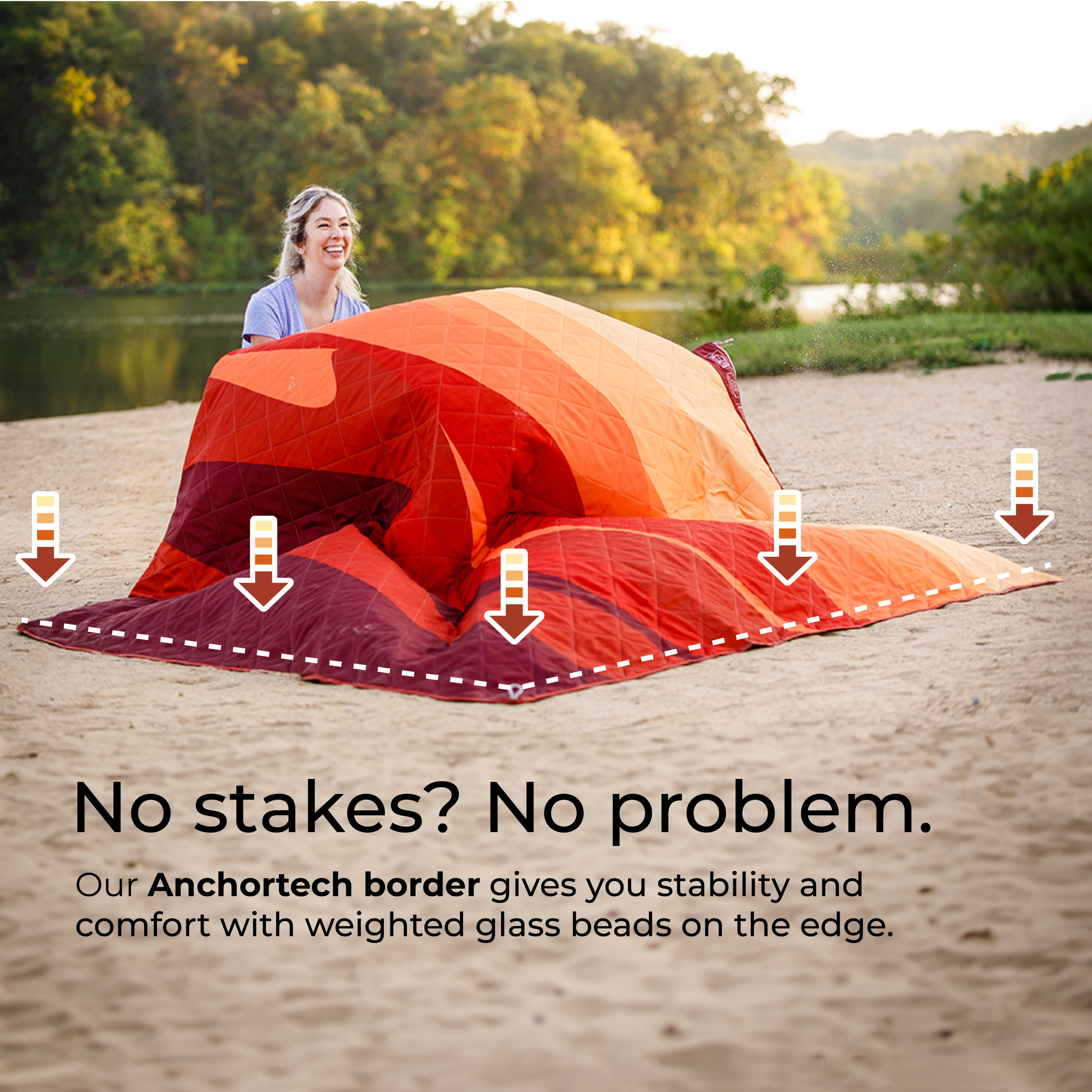 A smiling person sets up a red and orange weighted blanket on sandy ground near a river and lush greenery. The text on the image reads: "No stakes? No problem. Our Staydown Outdoor Travel Weighted Ground Blanket by CORE gives you stability and comfort with weighted glass beads on the edge.