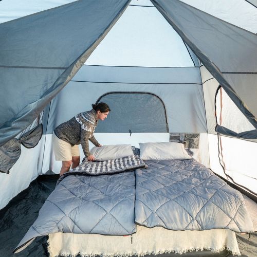 Person inside a CORE 10 person straight wall cabin tent with full rainfly setting up bed.