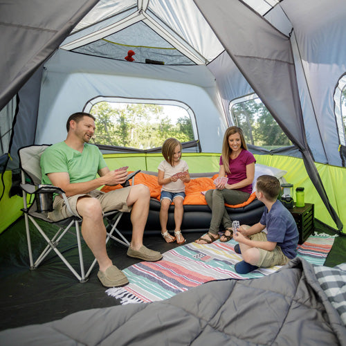 Family relaxing inside a CORE 10 person instant cabin tent with bedding, seating, and open windows while enjoying time together at camp.