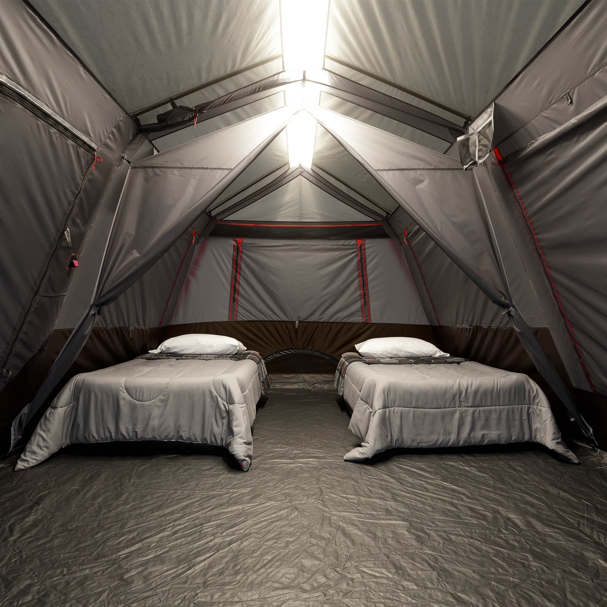 Two beds inside a large gray tent with a light on.