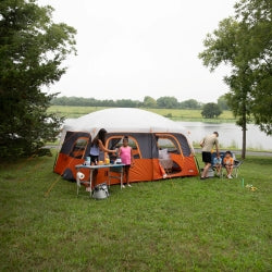 Family camping outdoors with a tent and picnic area by a lake.