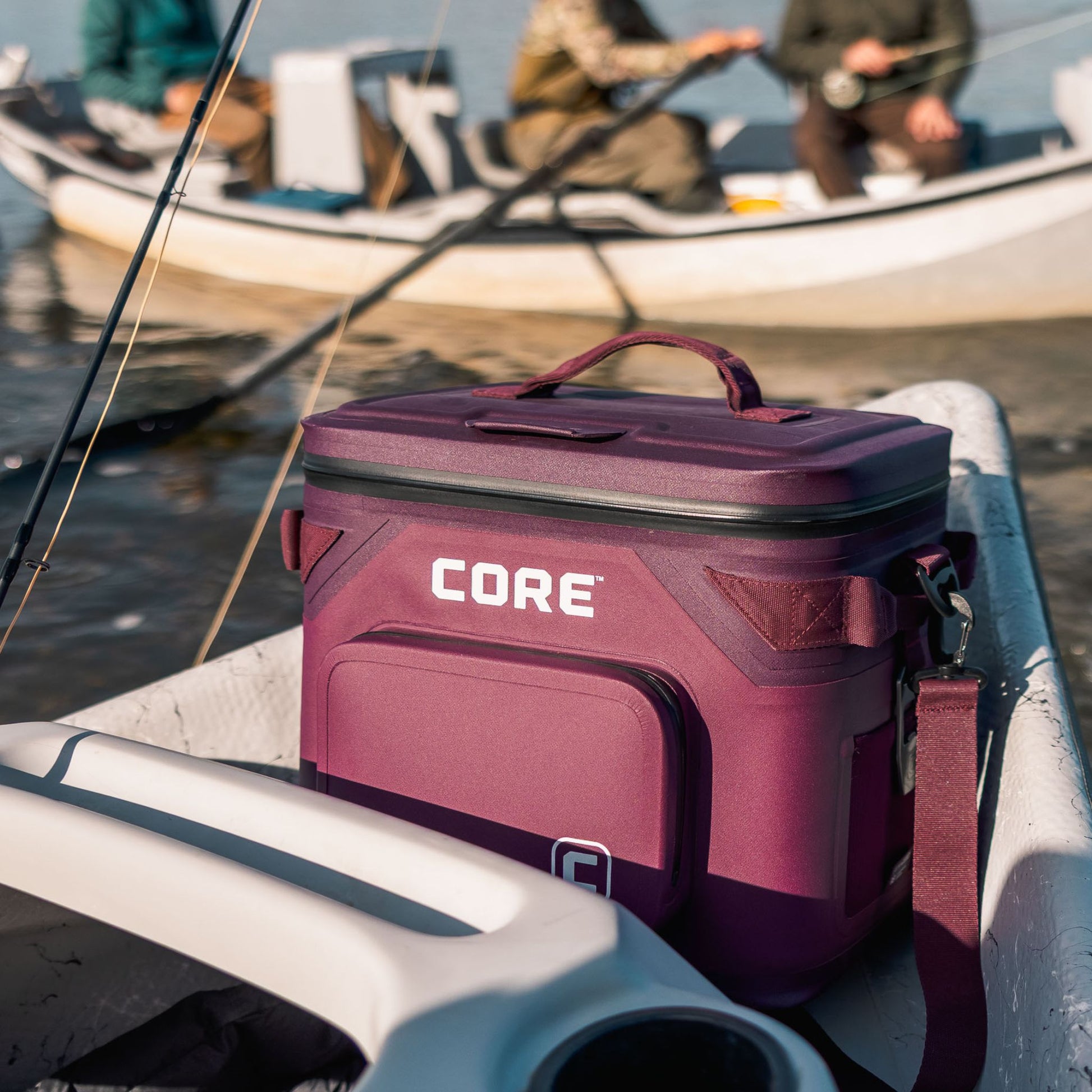 Maroon soft cooler bag with 'CORE' branding on a boat, with people fishing in the background.
