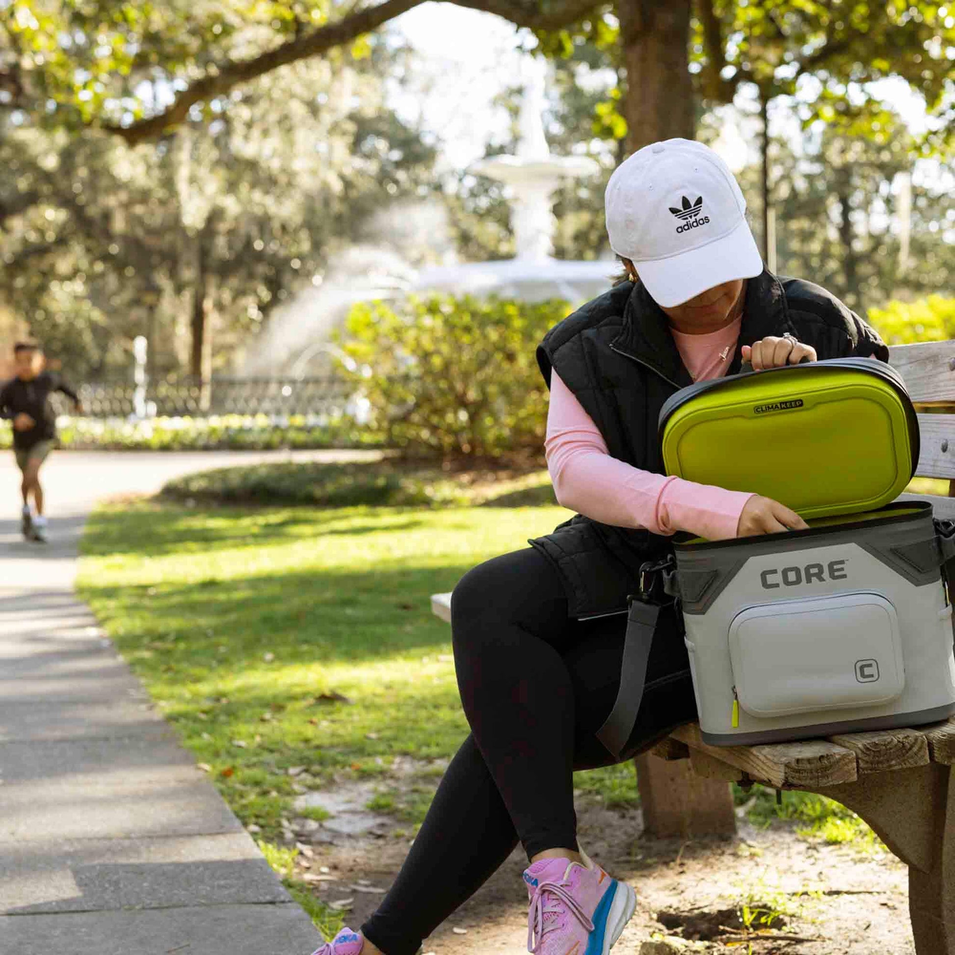 Person on park bench opening CORE 12 can Climakeep cooler in shadow gray with MagSnap lid and shoulder strap.